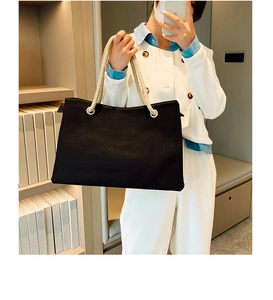 Detail of black canvas tote bag with woven cream rope handles held by a model