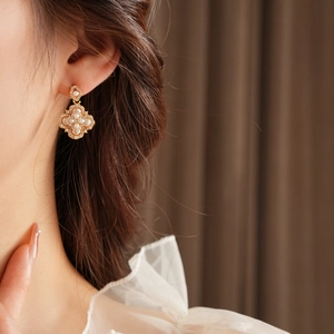 Gros plan d'une boucle d'oreille trèfle dorée avec perles et diamants sur un mannequin