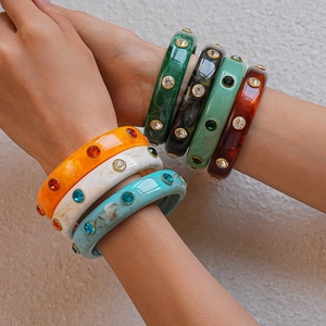 Detailed close-up of colorful acrylic bangles with embedded rhinestones in gold settings