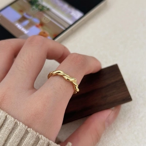 Close-up of a minimalist golden twisted rope ring worn on index finger with metallic luster