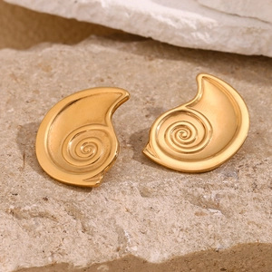 Detail of gold-plated cochlea-shaped earrings on a textured stone surface macro