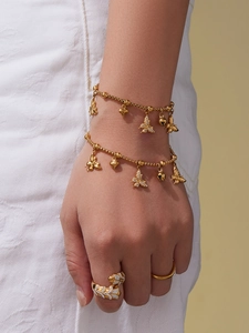 Detail van de gouden armband met vlinder en hart hangers aan de pols van het model