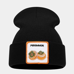 Detail of a black knitted beanie featuring a square patch with a persimmon fruit embroidery
