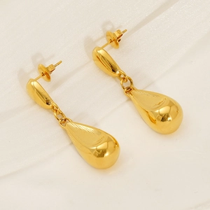Detailed view of polished 18K gold teardrop earrings on a soft textured fabric background