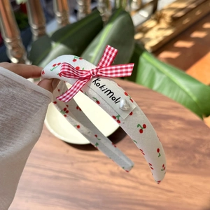 Detail of cherry pattern headband with red plaid bow and heart pearl embellishment