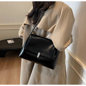 Detail of a black glossy chain shoulder bag paired with a classic beige trench coat