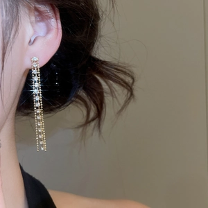 Dettaglio di eleganti orecchini a nappa dorata con strass scintillanti su modella donna