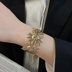 Nahaufnahme eines goldfarbenen, offenen Armreifs mit Sonnenmotiven am Handgelenk eines Models.