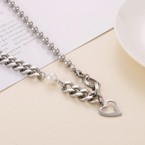 Détail du collier en acier titane argenté avec perle et pendentif cœur évidé sur fond beige