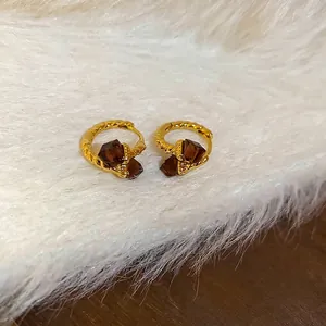Elegant gold twisted hoop earrings with brown square zircon stones on plush background