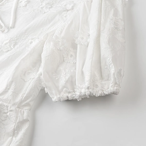 Detail of 3D floral embroidery and puffed sleeve design on a white summer top