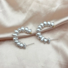 Close-up of C-shaped drop pearl earrings with gold accents on silk fabric