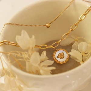Zweilagige Goldkette mit Bienen-Relief auf Perlmutt-Anhänger in einer Keramiktasse