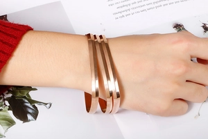 Close-up of three minimalist rose gold bangles stacked on a model's wrist with cozy decor