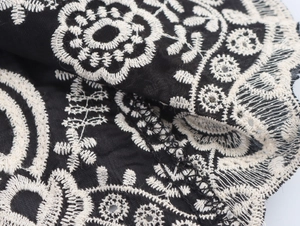 Detailed close-up of white floral embroidery on premium black fabric with lace edge