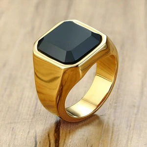 Anello da uomo in oro con zircone nero quadrato presentato su uno sfondo di legno