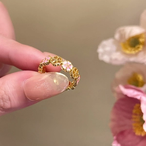 Close-up of 18k gold plated open ring with pink enamel flowers on a woman's finger