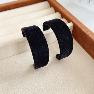 Macro detail of black velvet texture C-shaped hoop earrings in a jewelry tray