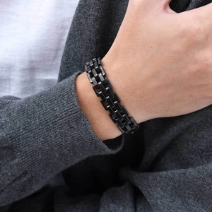 Close-up of black H-link stainless steel strap bracelet worn on wrist over a grey sweater