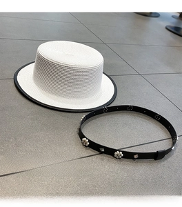 Detail of white woven straw boater hat with a removable pearl and metal studded leather strap