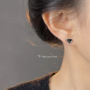 Close-up of heart-shaped black enamel stud earrings with silver arrow on model
