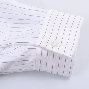 Close-up detail of white striped shirt cuff with a round button and breathable texture