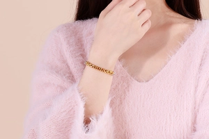 Close-up of a gold box chain bracelet on a model wearing a pink sweater