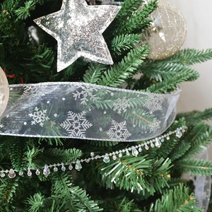 Detail of silver star topper and snowflake sheer ribbon on a green Christmas tree