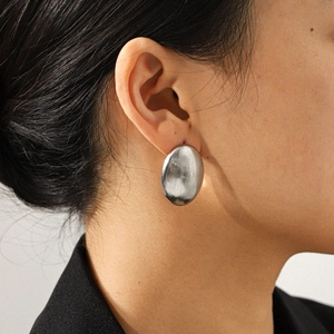 Gros plan d'une boucle d'oreille ovale en argent au fini brossé portée par un mannequin