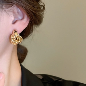 Nahaufnahme eleganter goldener Metallknoten-Ohrstecker an einem Modell mit Glanzfinish