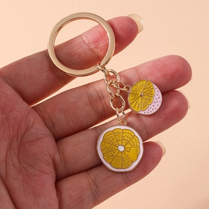 Detail of yellow enamel lemon slice charms on a golden keychain held by hand