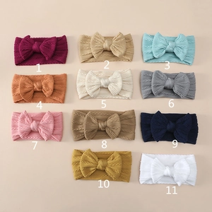 Flat lay of 11 multi-colored knitted baby bow headbands with soft ribbed texture