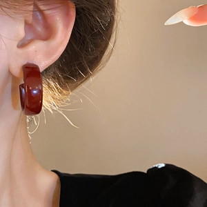 Close-up of a woman wearing deep red C-shaped resin hoop earrings with glossy finish