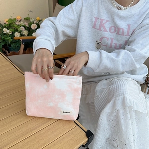 Detail of a tie-dye canvas makeup bag with Sozakka brand label on a wooden table
