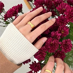 Close-up of elegant gold bow ring and minimalist band on finger with red floral background