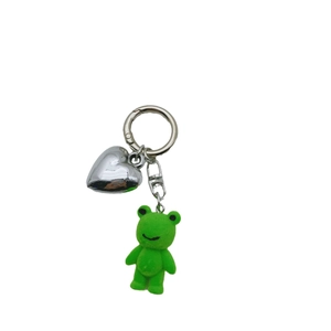 Cute green flocked frog keychain with silver metal heart pendant on white background
