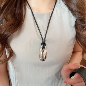 Close-up of geometric oval pendant on black leather cord worn over a light grey top