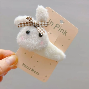 Detail of handmade plush white bunny hair clip with a brown plaid bow on display card