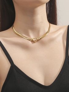 Detailed close-up of a gold heart pendant necklace on a sleek snake chain shown on a model