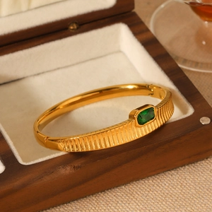 Close-up of gold stainless steel bangle with green stone in a wooden jewelry box