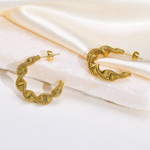 Detail view of gold C-hoop earrings with textured wire wrap on marble background