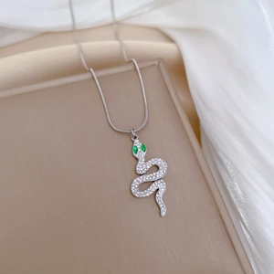 Close-up of silver snake pendant necklace with green crystal eyes on soft beige fabric