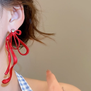 Macro side view of elegant red ribbon bow earrings with a single rhinestone on the ear