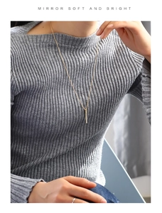 Close-up of gold bamboo pendant necklace with crystals worn over a grey sweater