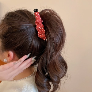 Détail d'une pince à cheveux en tissu rouge à pois sur une coiffure en queue de cheval
