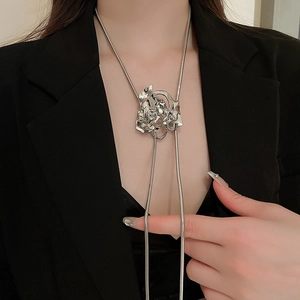 Detail view of a silver metallic rose flower pendant necklace on a black suit jacket