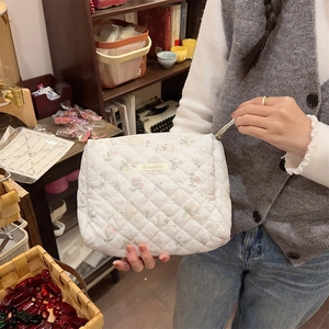 Gros plan détaillé d'une trousse à maquillage blanche matelassée tenue par un mannequin