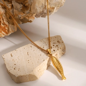 Close-up of golden stainless steel necklace with fish pendant on stone