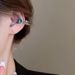 Gros plan d'un ear cuff argenté avec un grand cristal bleu mer et des strass blancs
