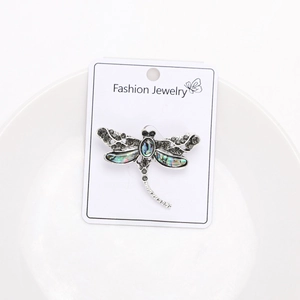 Detailed macro view of dragonfly brooch with abalone shell and rhinestones in white dish